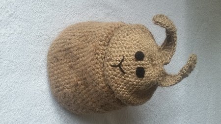 Gehäkelter brauner Korb in Käferform mit aufgesticktem Gesicht und Fühlern auf hellem Hintergrund.