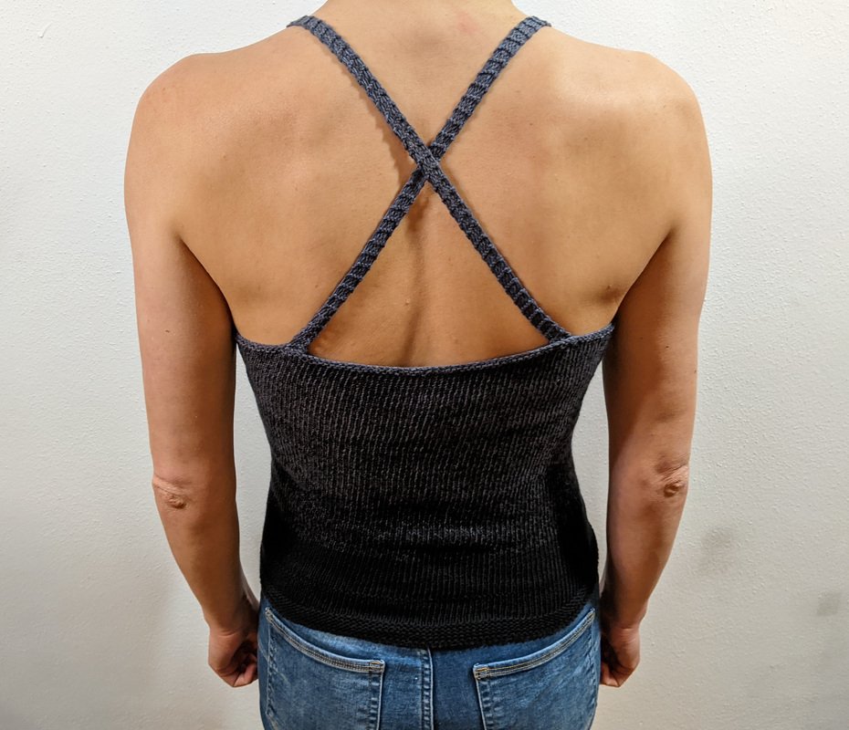 Dunkelgraues geripptes Damen-Top mit gekreuzten Trägern, Rückenansicht, getragen zu blauen Jeans vor heller Wand