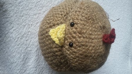 Kleines rundes gehäkeltes Küken mit gelbem Schnabel und rotem Kamm