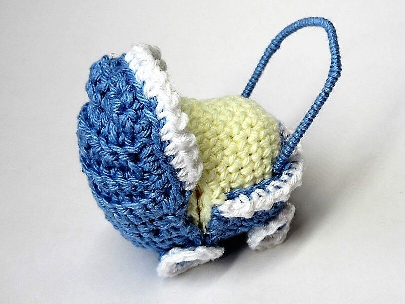 Gehäkelter Mini-Kinderwagen in Blau und Weiß mit hellgelbem Innenraum und geschwungenem Griff
