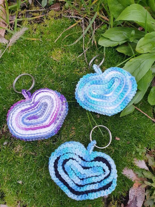 Drei spiralgearbeitete Häkelherzen mit Schlüsselringen auf Gras