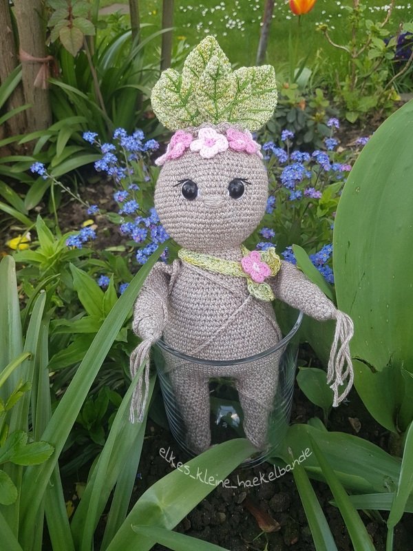 Gehäkelte Alraune-Amigurumi-Figur mit Blätterkrone und rosa Blüten, in einem Glas im Garten