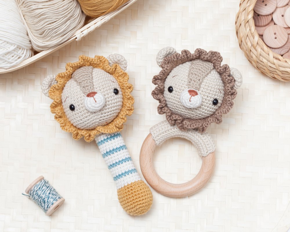 Wooden teether with crocheted lion head next to a striped crocheted lion rattle