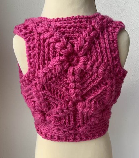 Rückenansicht einer leuchtend pinken, gehäkelten Kinderweste auf einer Schaufensterpuppe.