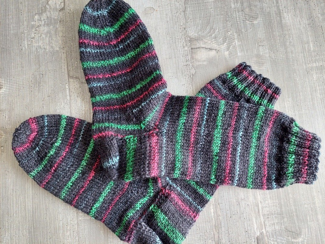 Gestricktes Paar Herrensocken in dunkelgrau mit grünen, pinken und hellblauen Streifen auf hellem Holzuntergrund