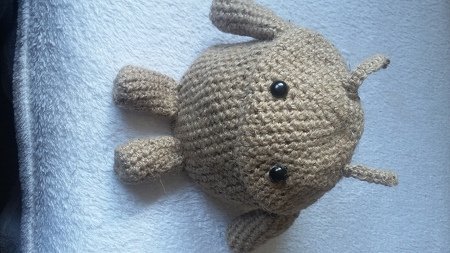 Beige, rund gehäkelte Amigurumi-Figur mit vier kurzen Beinchen und schwarzen Knopfaugen auf hellem Untergrund