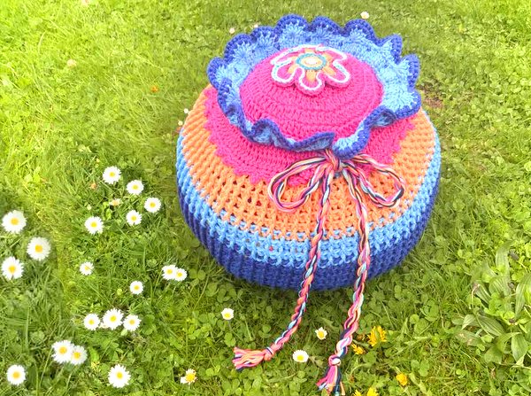 Rundes gehäkeltes Bodenkissen mit Rüsche, Blumenapplikation und Zierkordel auf Gras mit Gänseblümchen