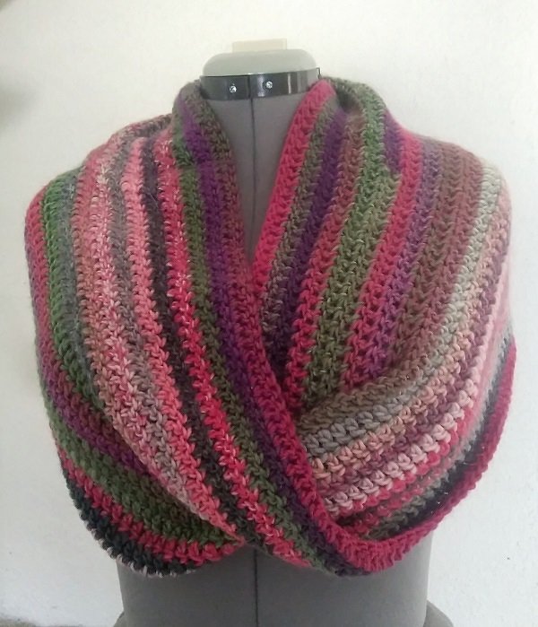 Mehrfarbiger gehäkelter Loop-Schal auf einer Schneiderpuppe in Rosa, Lila und Olivgrün.