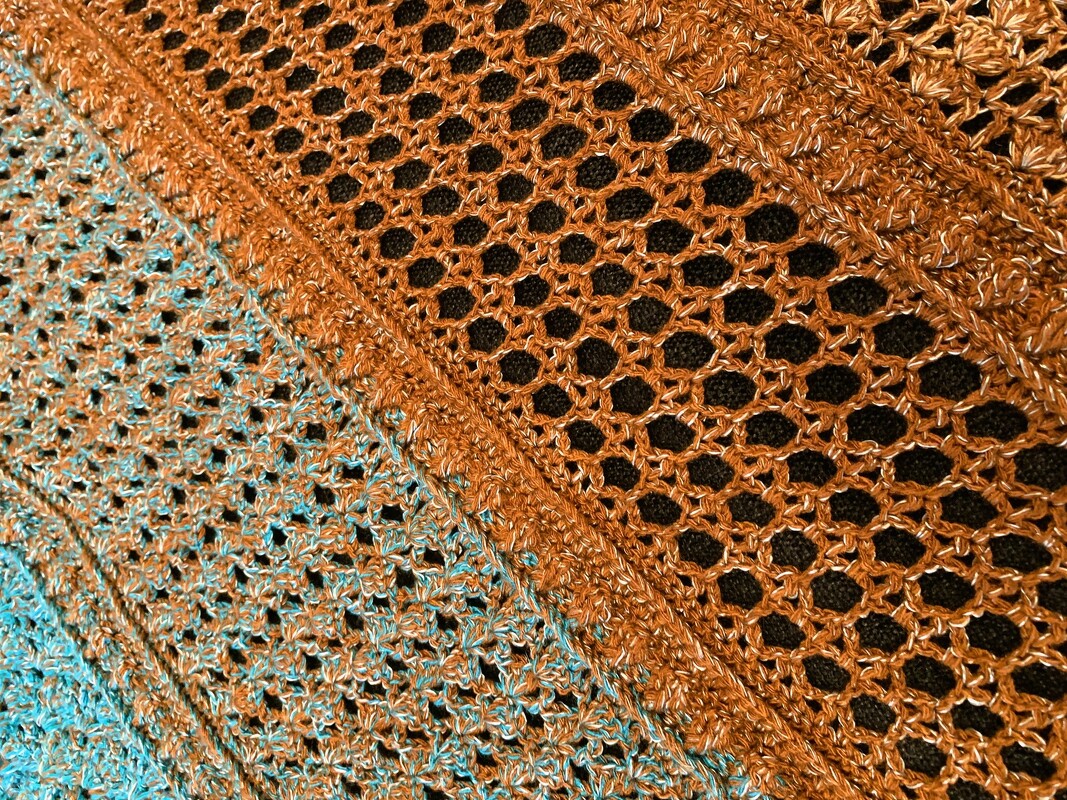 Close-up of openwork crocheted triangle shawl in orange-brown to blue-turquoise gradient