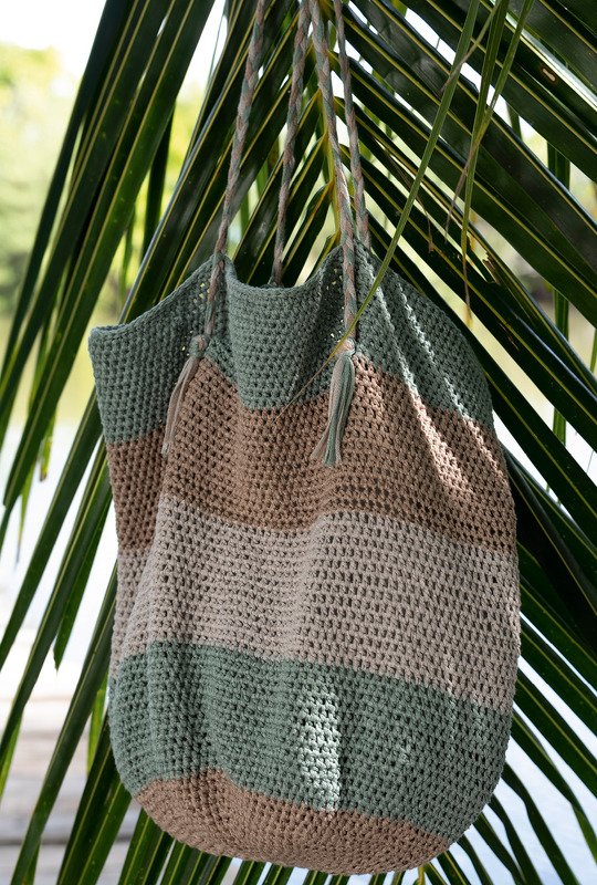 Gestreifte gehäkelte Tasche in Grün und Beige, hängend an einem Palmenblatt