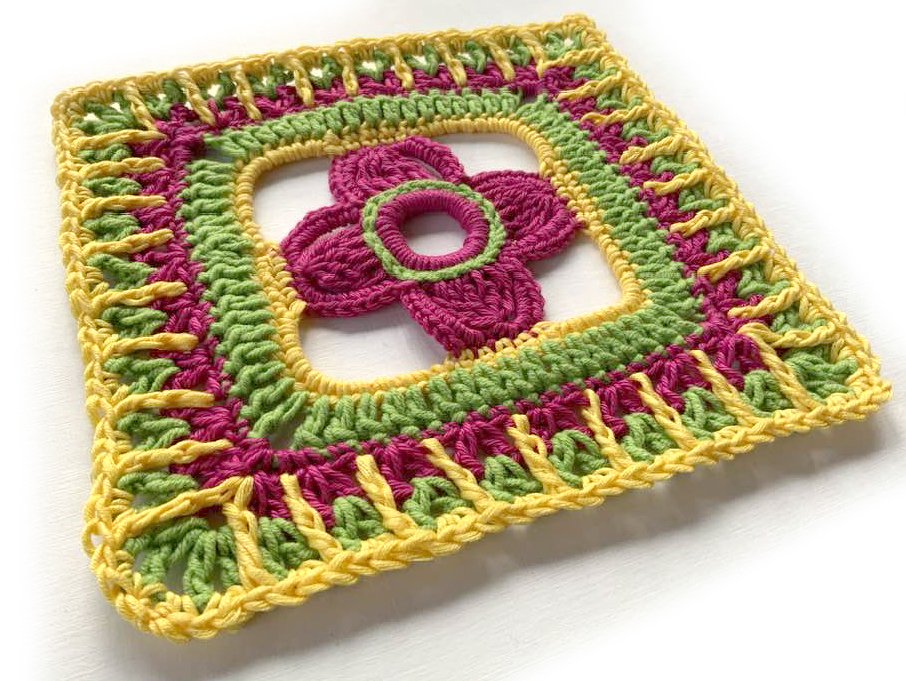 Gehäkeltes quadratisches Motiv mit zentraler Blüte in Pink, Hellgrün und Gelb