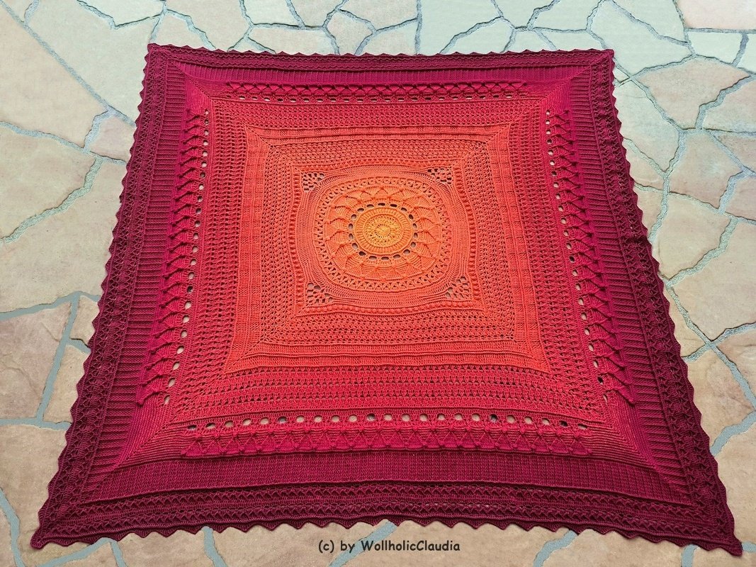 Quadratische Häkeldecke in Orange bis Dunkelrot mit Mandala-Motiv auf hellem Boden