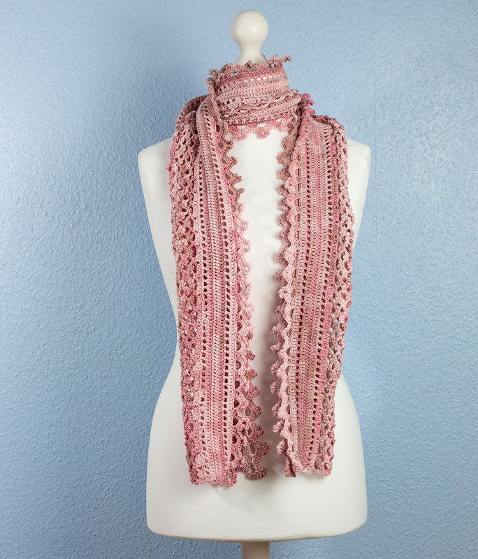 Handgehäkelter Schal in Rosatönen mit Lochmuster und gewellter Kante auf einer Schneiderpuppe.