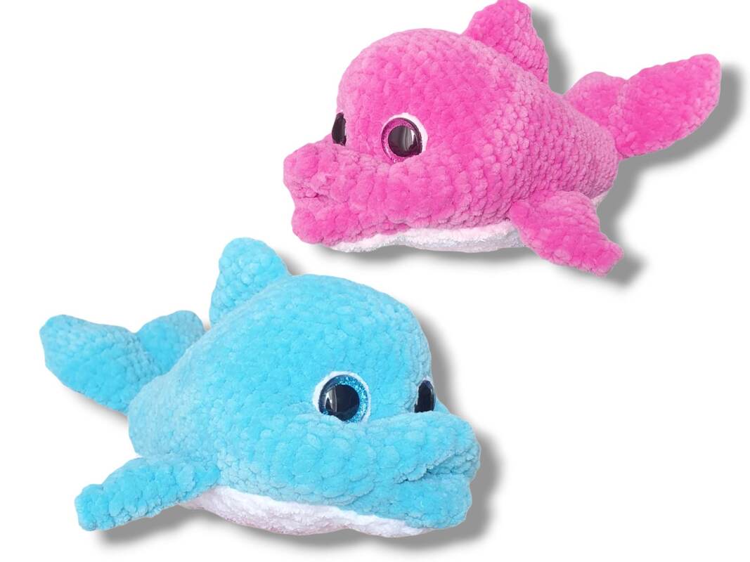 Two crocheted amigurumi dolphins, one pink and one blue, with plush textured yarn and round glossy eyes