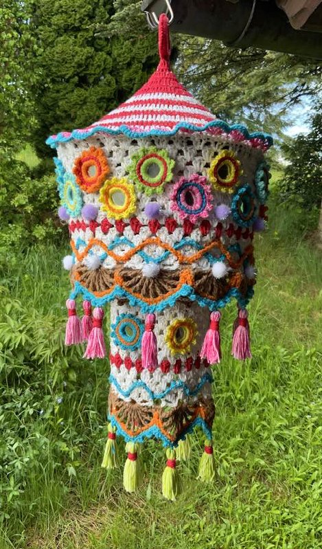 Handgearbeiteter, farbenfroher Häkel-Lampion mit floralen Mustern, Pompons und Quasten, im Grünen hängend