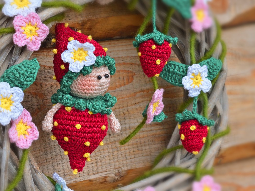 Gehäkelter Türkranz mit Erdbeer-Wichtel, roten Erdbeeren und farbigen Blüten auf Holzhintergrund.