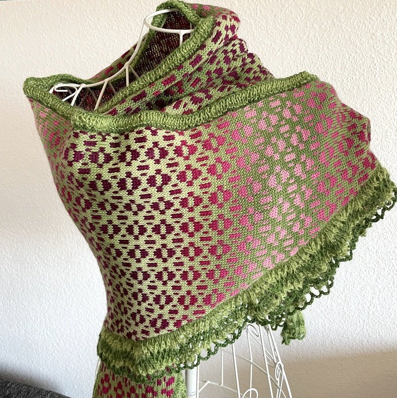 Gestricktes Dreieckstuch in Grün- und Rosatönen mit geometrischem Muster und grüner Kante, drapiert auf einer Schneiderpuppe
