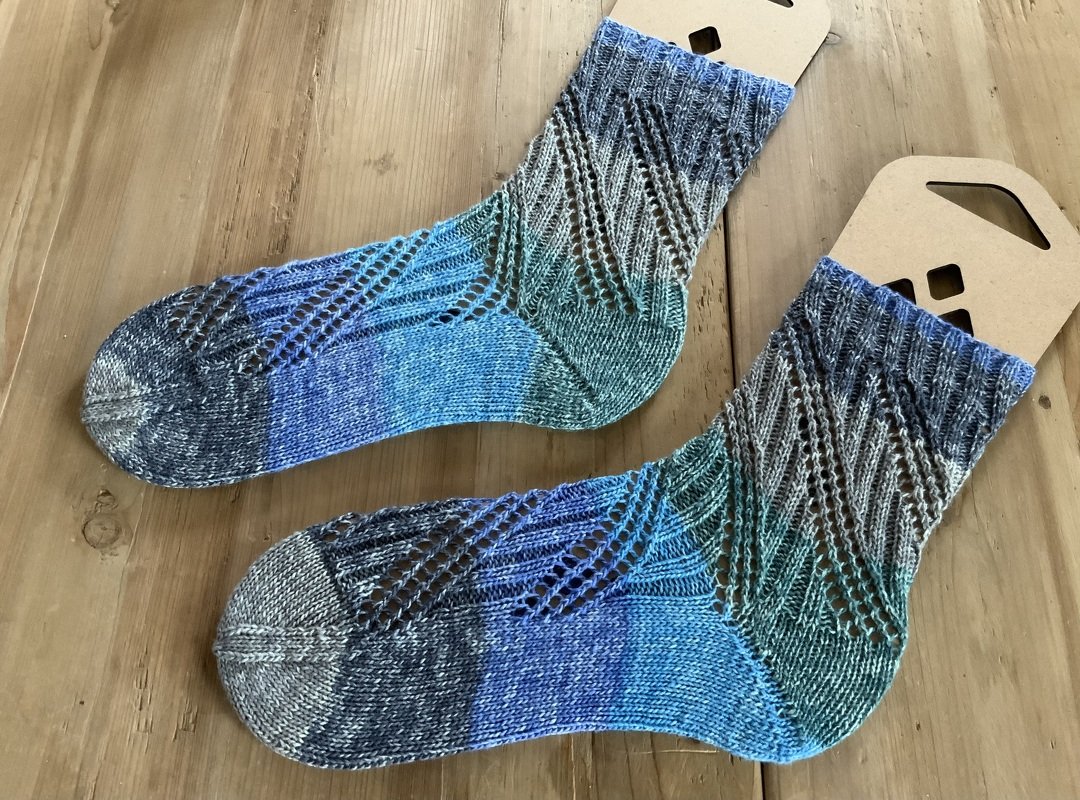 Paar handgestrickter Socken in Blau-Grün mit diagonalem Ajourmuster auf Holzuntergrund