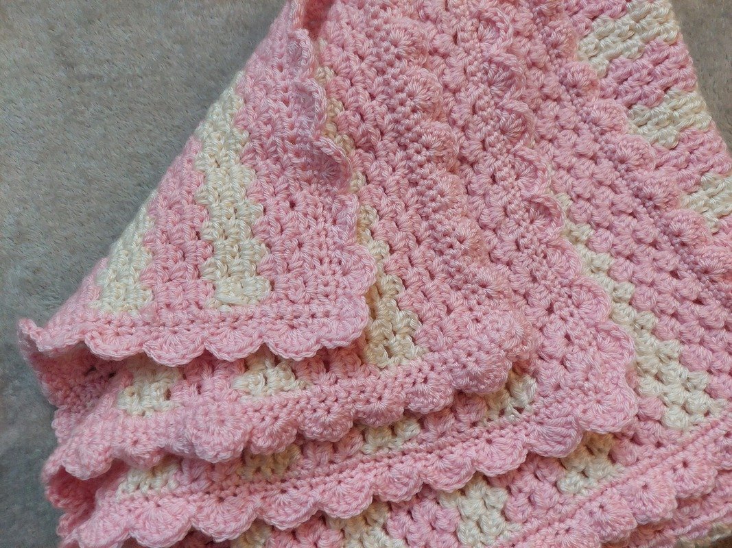 Gefaltete rosa-creme Babydecke mit Streifenmuster und Muschelkante