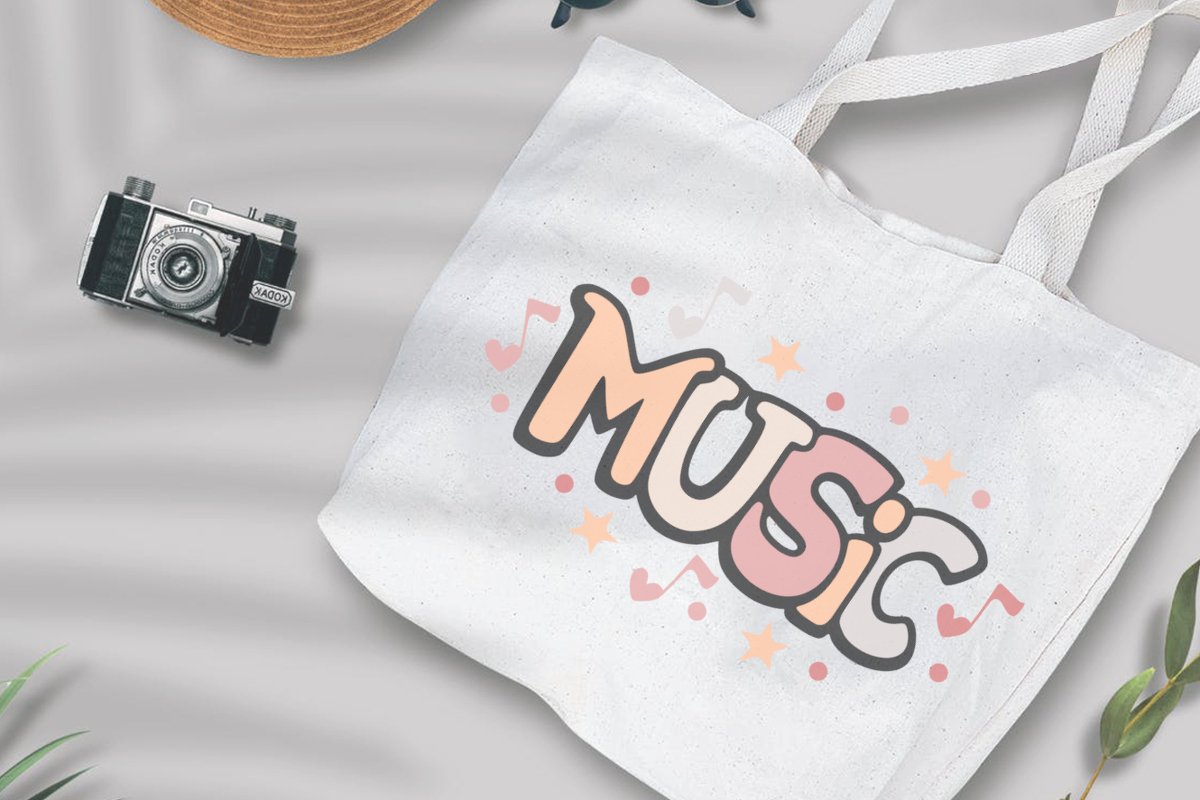 Weiße Stofftasche mit Music-Schriftzug, Noten und Sternen in Pastellfarben, daneben eine Retro-Kamera und ein Strohhut.