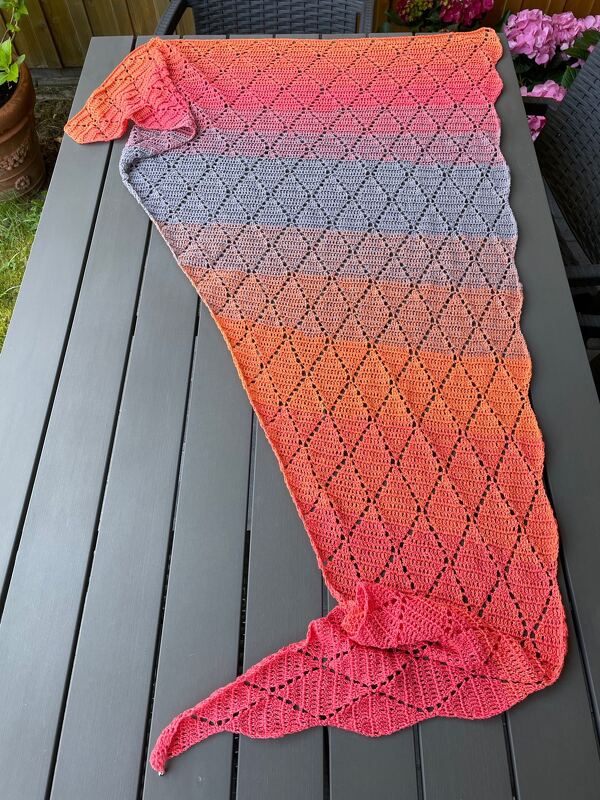 Asymmetrisches Dreieckstuch gehäkelt mit Rautenmuster und Farbverlauf rosa-grau-orange auf Außenmöbel gelegt