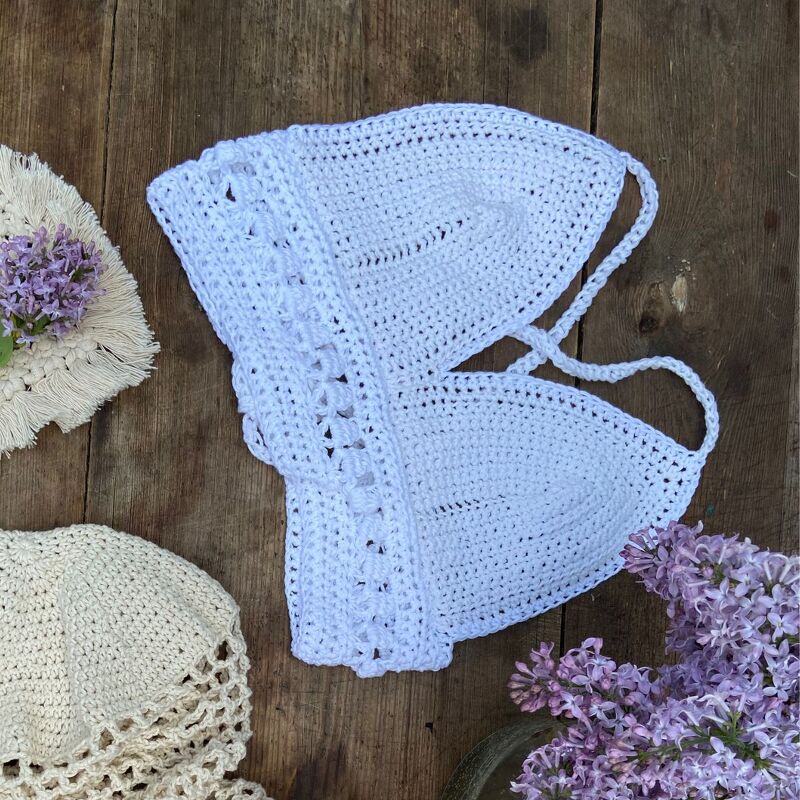 Weißes gehäkeltes Dreieckstop auf hellem Holz mit lila Flieder