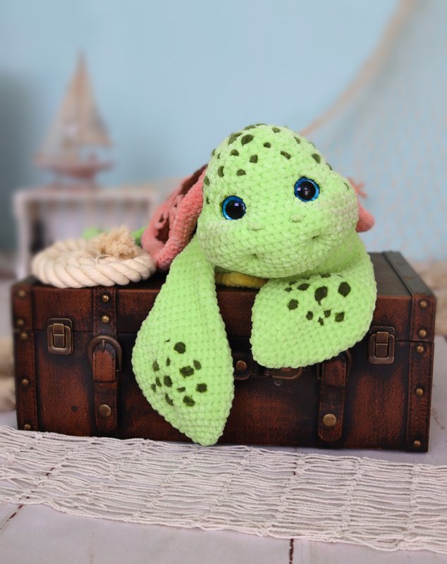 Light green crocheted amigurumi sea turtle with blue eyes and dark green spots on a brown suitcase