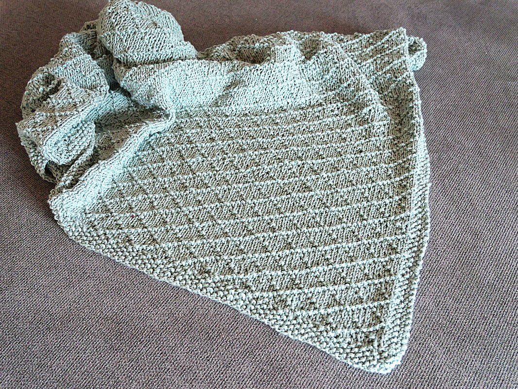 Nahaufnahme einer mintgrünen gestrickten Babydecke mit Rautenmuster auf neutralem Untergrund.