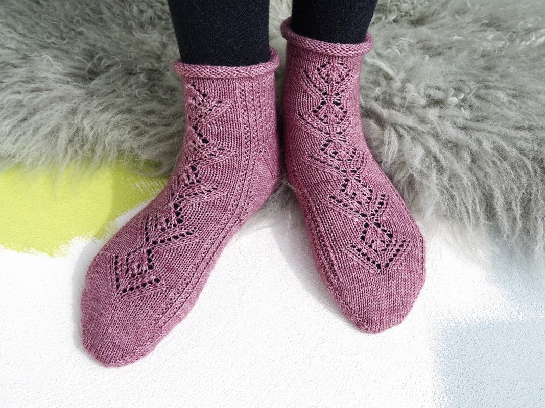 Rosafarbene gestrickte Socken mit Ajourmuster auf grauem Teppich.
