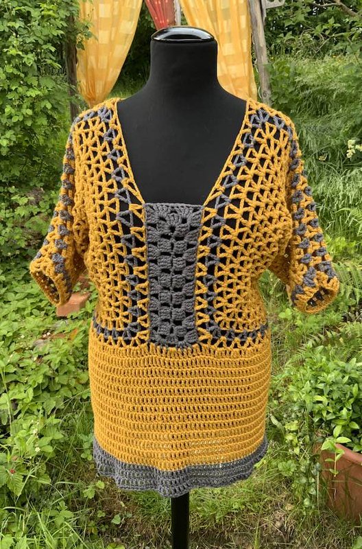 Gehäkelte Damen-Tunika in Senfgelb und Grau auf Schneiderbüste; offenes Netzoberteil, mittiges Granny‑Panel und dicht gehäkelter Unterteil