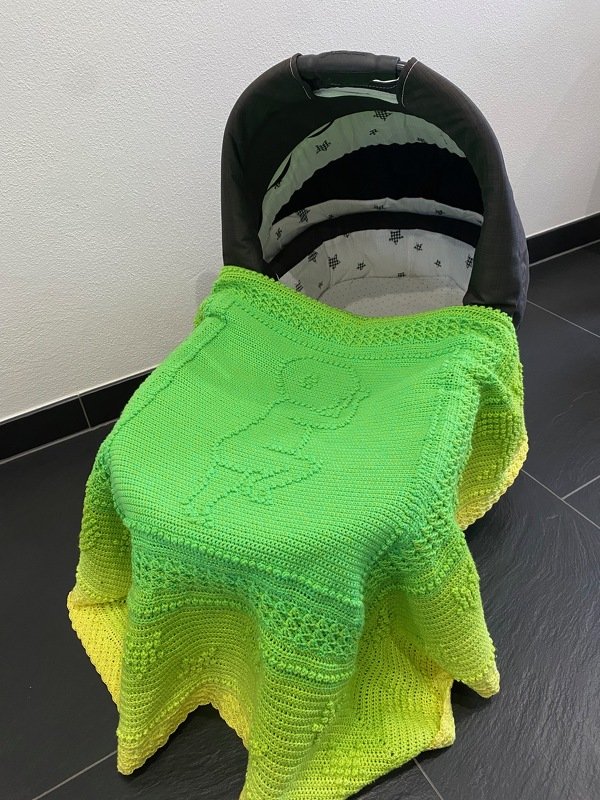 Kompakt gehäkelte Babyschalen‑Decke in grün‑gelbem Verlauf mit mittigem Reliefmuster