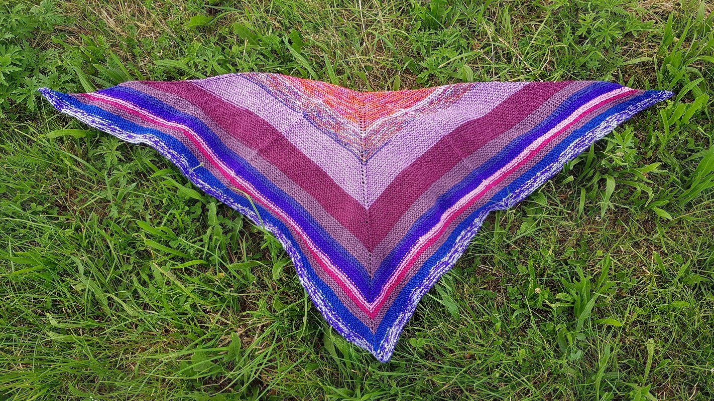 Gestricktes Dreieckstuch mit bunten Streifen in Lila, Pink und Blau auf Gras