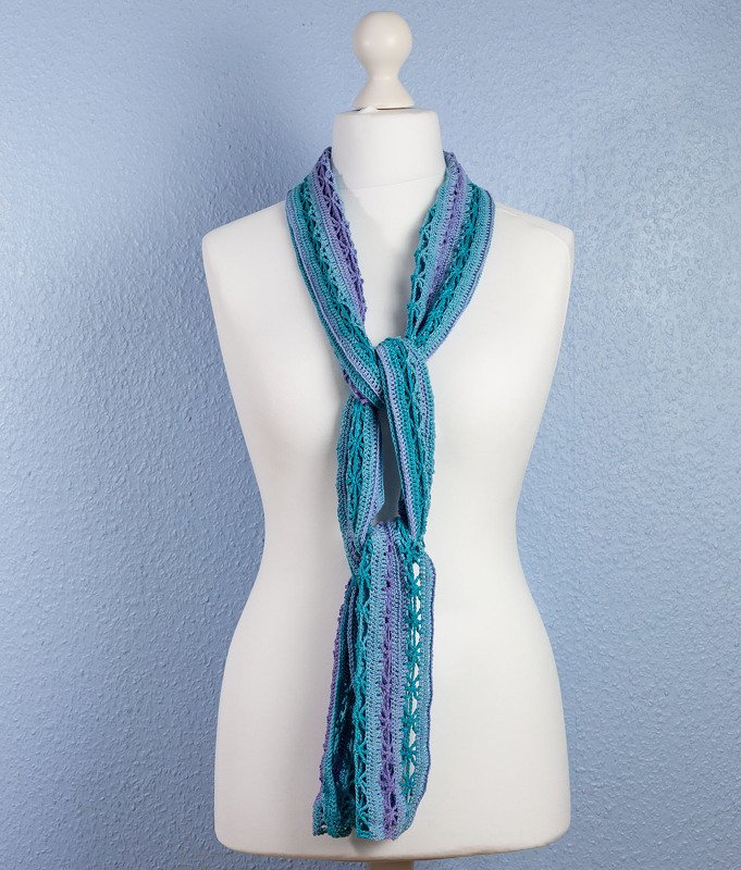 Schmaler gehäkelter Schal in Türkis und Lila, locker geknotet an einer Schneiderpuppe