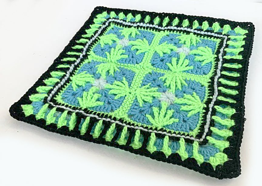 Gehäkeltes Quadrat in Neongrün, Hellblau und Schwarz mit palmenblattähnlichem Muster und gezacktem Rand.