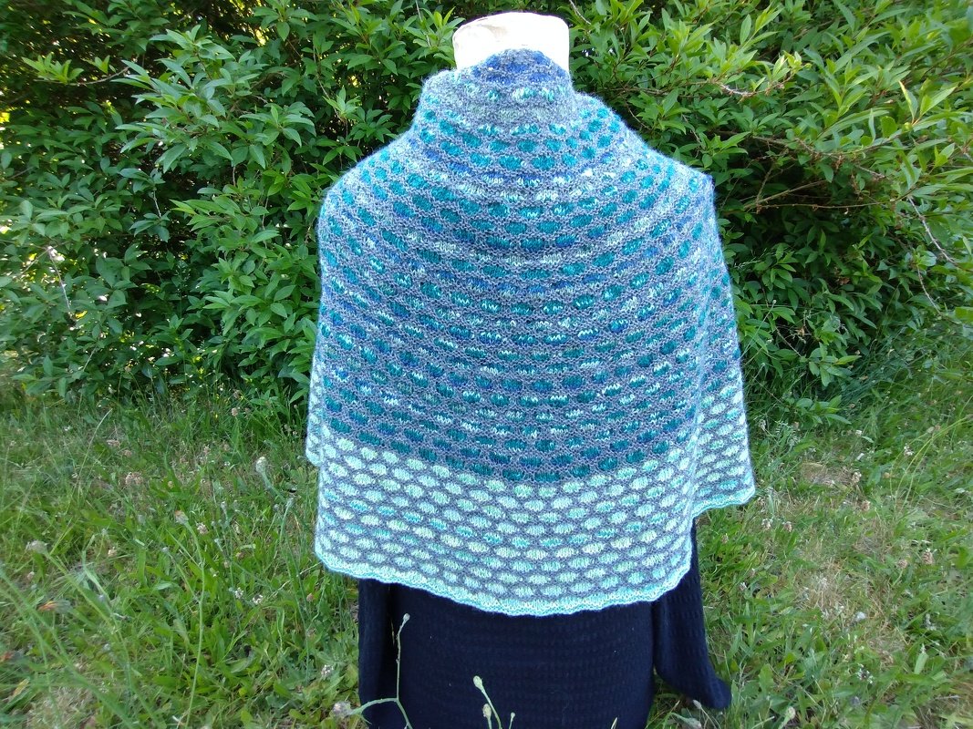 Gestricktes Halbrundtuch in Blau- und Petroltönen mit Strukturmuster, Rückansicht auf einer Puppe vor grünen Pflanzen