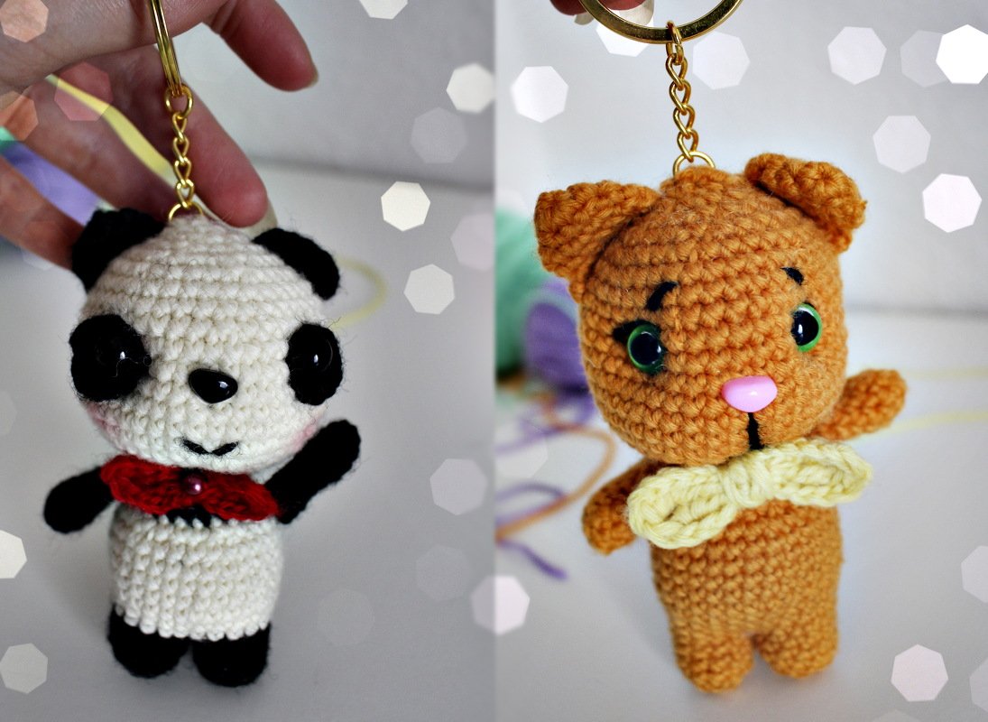 Hand hält zwei gehäkelte Amigurumi-Schlüsselanhänger: Panda und Katze.