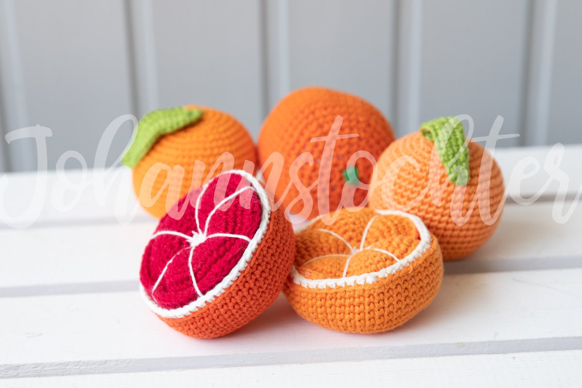 Gehäkelte Orangen: drei ganze Früchte und zwei halbierte Orangenhälften auf hellem Untergrund