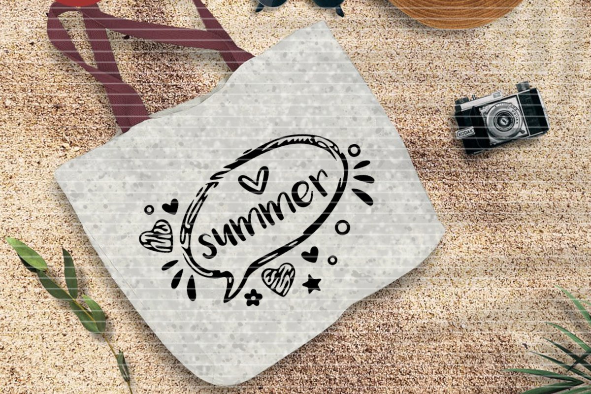 Helle bedruckte Stofftasche mit dem Schriftzug 'summer' liegt auf sandigem Boden, umgeben von sommerlichen Gegenständen.