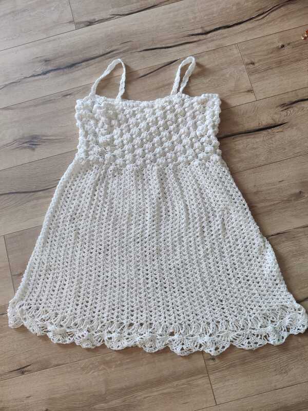 Weißes gehäkeltes Damenkleid mit dünnen Trägern, Noppenoberteil und Muschelsaum auf Holzfußboden
