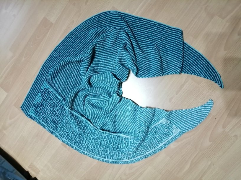 Türkisfarbenes gestricktes Dreieckstuch mit Streifen und geometrischem Randmuster auf hellem Holz