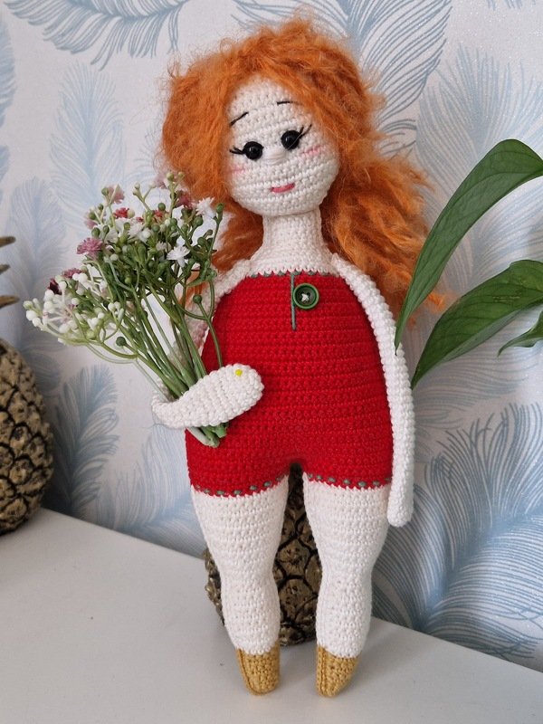 Gehäkelte Amigurumi-Puppe mit orangefarbenen Haaren, rotem Outfit und Blumenstrauß