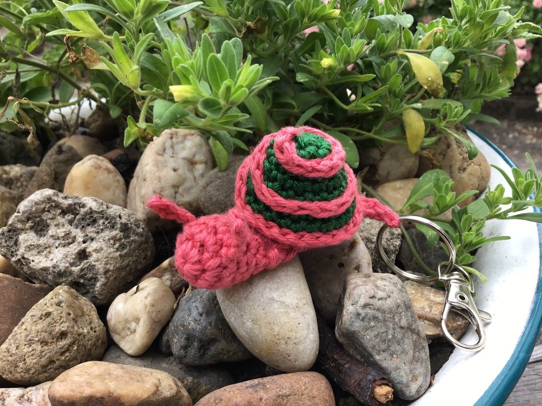 Kleiner schnell gehäkelter Schnecken‑Schlüsselanhänger mit Metallring und rosa‑grüner Spirale