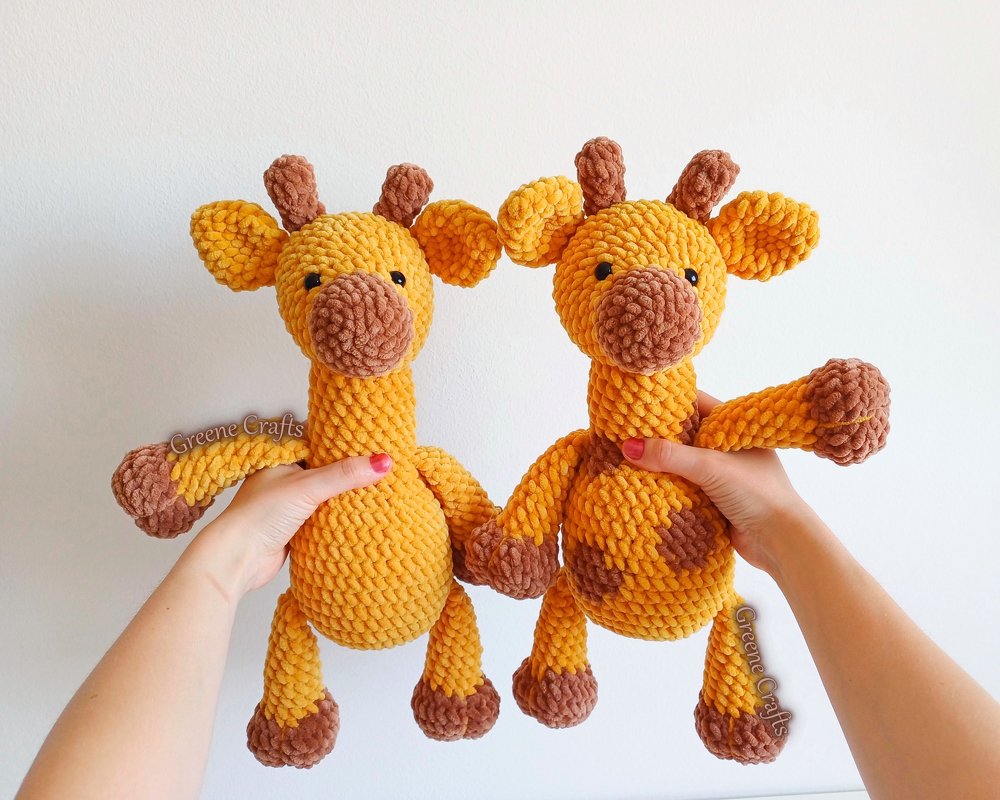 Hands holding two yellow and brown crocheted amigurumi giraffe toys, one spotted