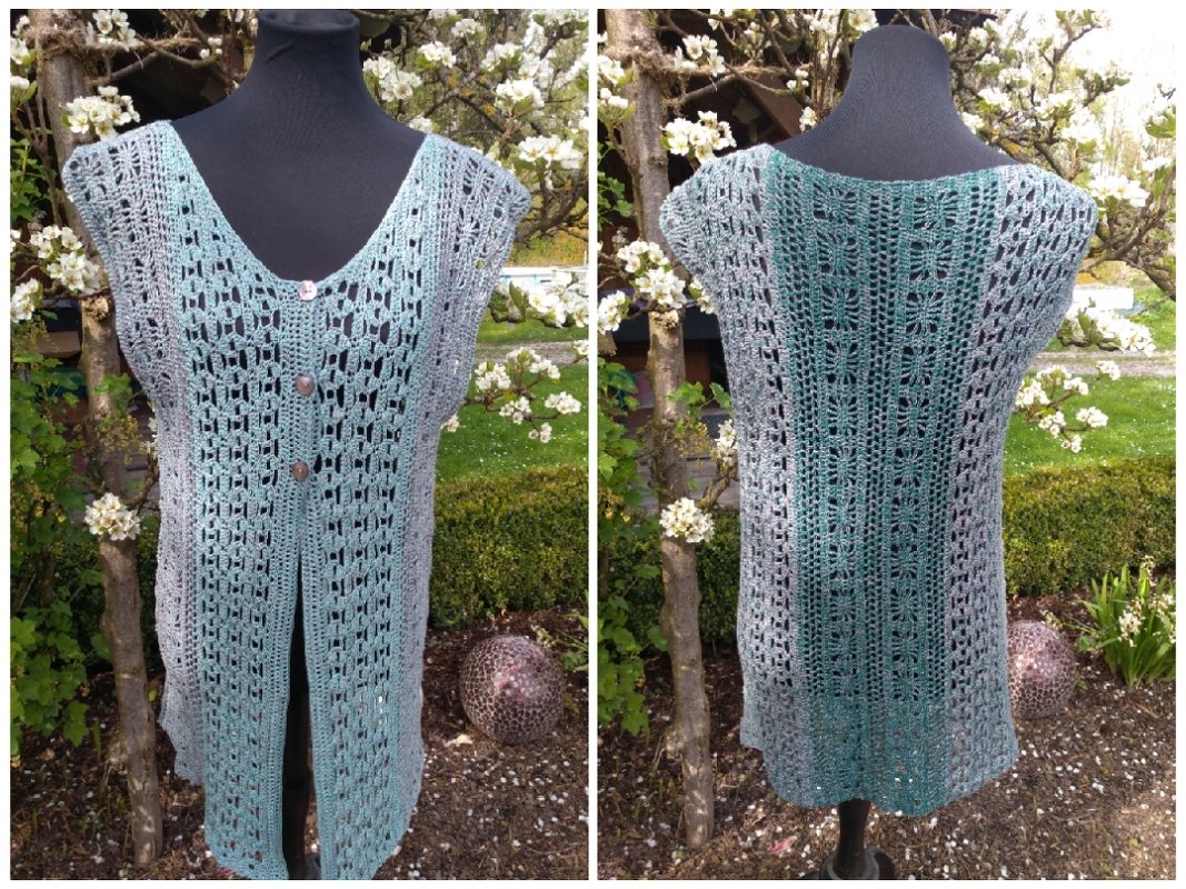 Lange ärmellose Häkelweste in Mintgrün und Grau mit Lochmuster und drei Knöpfen auf Schaufensterpuppe vor blühendem Baum