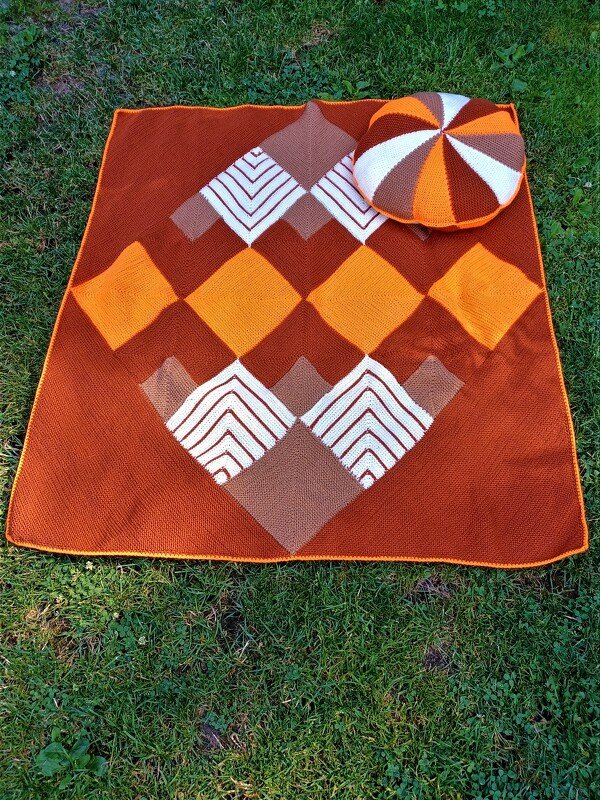 Gestrickte Decke mit Rautenmuster und rundes Kissen auf Rasen