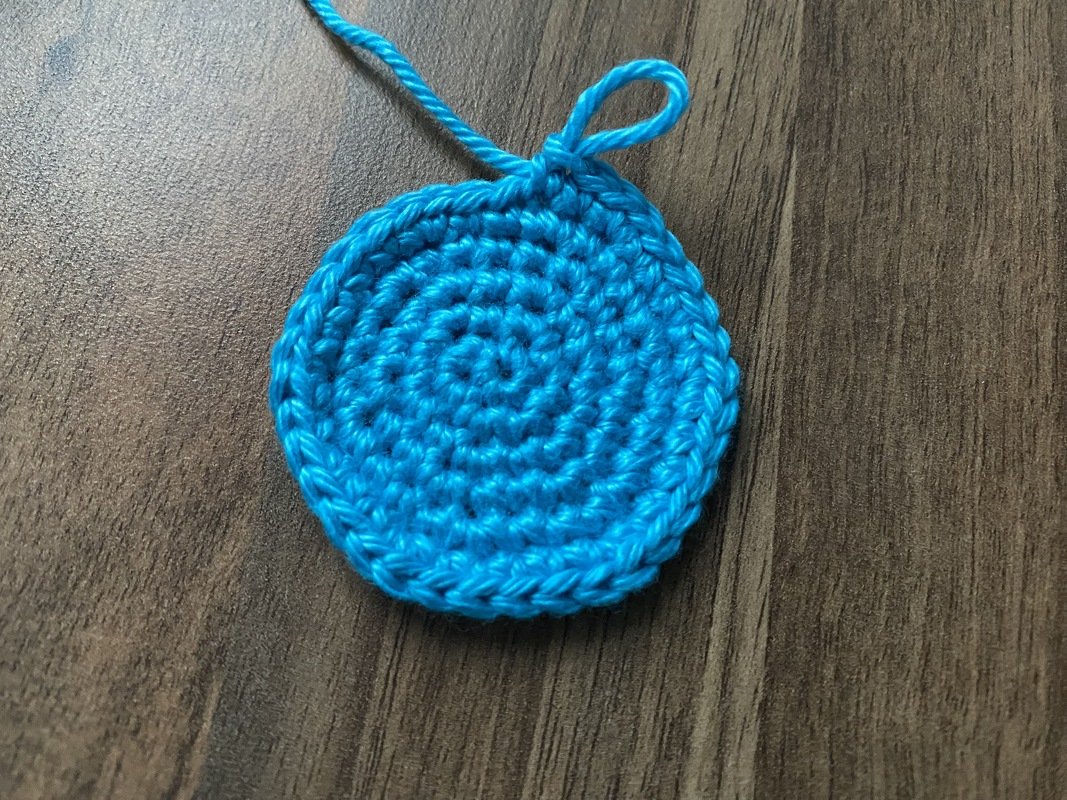 Blauer gehäkelter Kreis aus Garn auf dunklem Holztisch