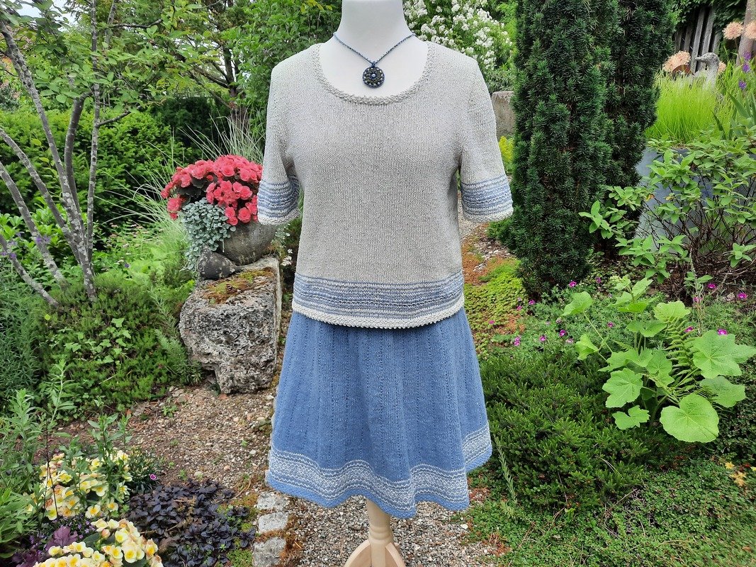 Schaufensterpuppe mit hellgrauem gestricktem Kurzarmtop und blauem ausgestelltem Rock im Garten