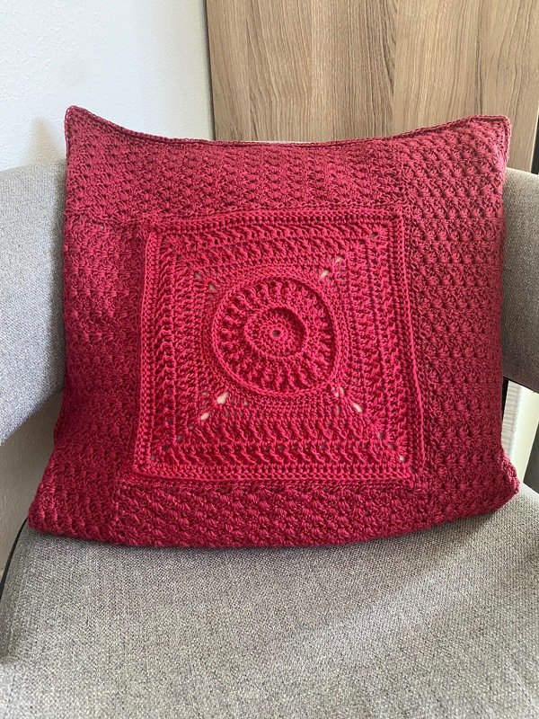 Dunkelrotes gehäkeltes Kissen mit Mandala-Motiv auf grauem Stuhl