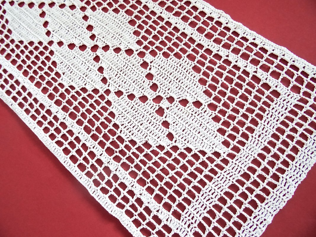 weiß gehäkelter Tischläufer im Filetmuster mit Blattmotiv auf rotem Untergrund