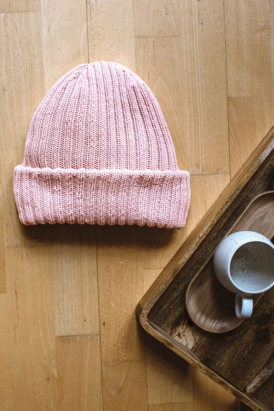 Rosa gerippte Beanie mit Umschlag auf Holzboden neben Holztablett und Keramikbecher